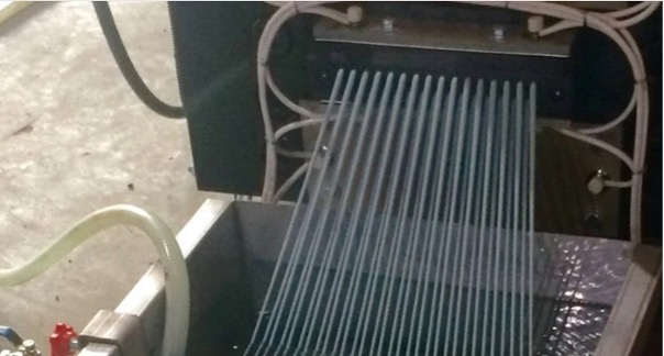 Extruded recycled plastic strands emerging from the die and entering a water cooling bath for the spaghetti-cutting pelletizing process.