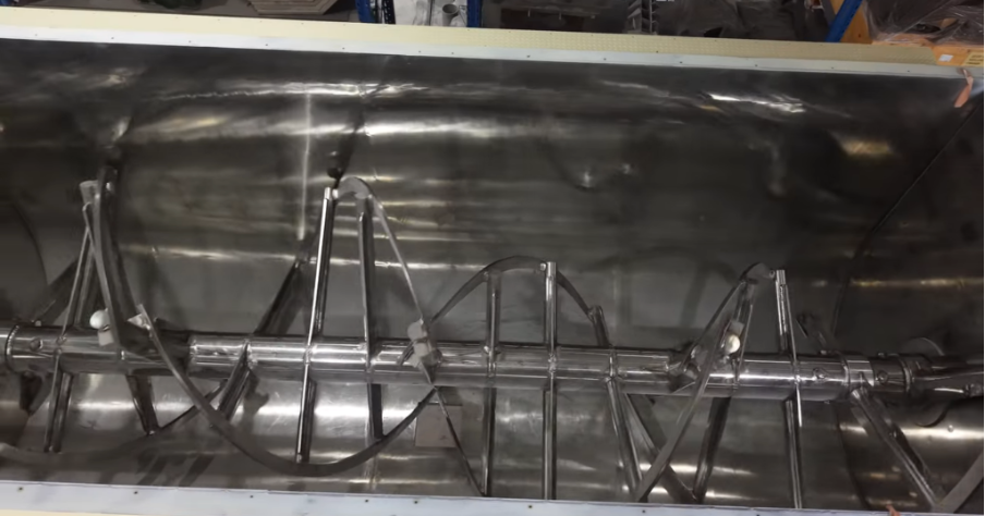Unlike gravity-fed vertical silos, horizontal ribbon mixers utilize active axial and radial counter-flow to achieve precision micro-dispersion across large batches.